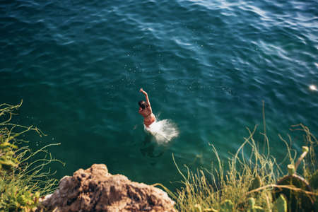 Woman jumping off cliff into the sea. Summer fun lifestyle.