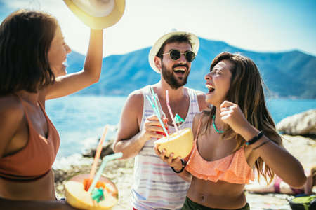 Group of friends having fun on the beach dancing and drinking cocktails.の写真素材