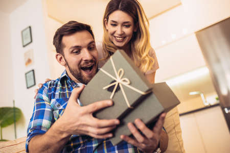 Romantic couple at home. Woman giving a present to her boyfriend.