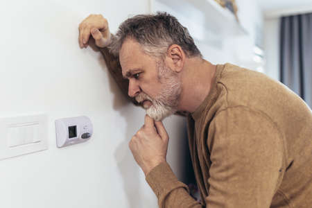 Mature Man Adjusting Central Heating Temperature At Home On Thermostat