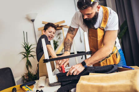 Smiling father is teaching his son upholstery at home, having fun.