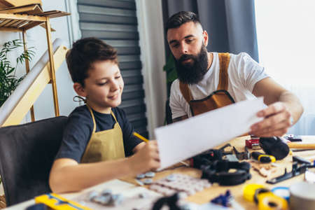 Smiling father is teaching his son of working with wood at home.の写真素材