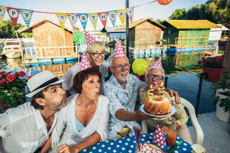 Senior people celebrating birthday in the cottage on the river having fun.
