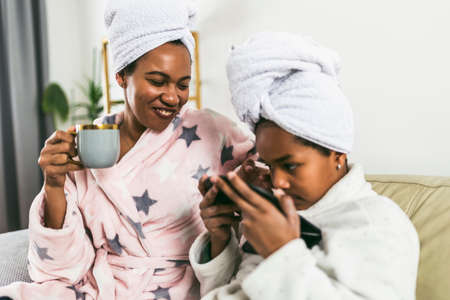 Mother Daughter Beauty Treatments. Caring Black Mom Teaching Little Girl Self-Care At Home, Sitting In Bathrobes.の写真素材