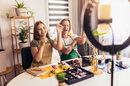 Mother and daughter accessories designers making handmade jewelry in studio workshop and recording video. Fashion, creativity and handmade concept.の写真素材