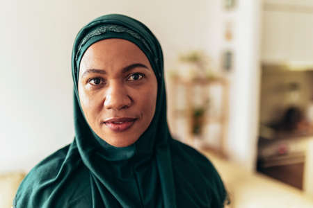Muslim woman in hijab looking at camera at home.の写真素材