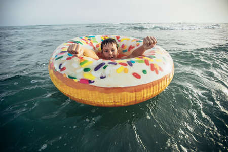 Joyful child on inflatable ring ride on breaking wave. Travel lifestyle, swimming activities. Selective focusの写真素材