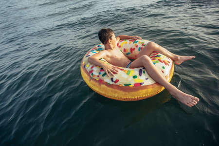 Joyful child on inflatable ring ride on breaking wave. Travel lifestyle, swimming activities. Selective focusの写真素材