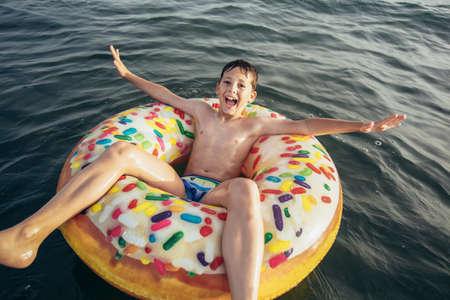 Joyful child on inflatable ring ride on breaking wave. Travel lifestyle, swimming activities....