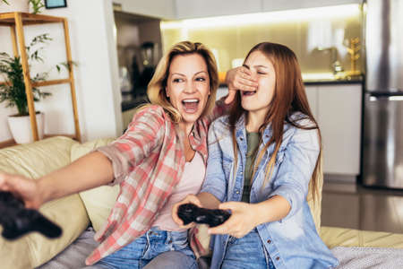 Mother and daughter playing video games together. Home leisure lifestyle.の写真素材