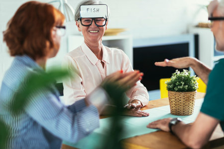 Senior friends with pieces of paper on foreheads sitting at dining table and playing guessing game