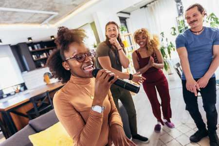 Group of young multicultural friends having party singing song using microphone at home.の写真素材