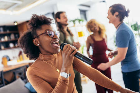 Group of young multicultural friends having party singing song using microphone at home.