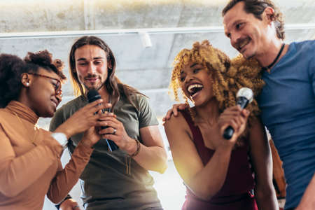 Group of young multicultural friends having party singing song using microphone at home.