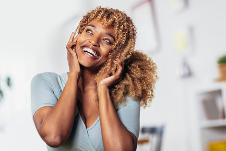 Portrait of smiling young black woman curly hair and bright eyes listening music with headsetの写真素材