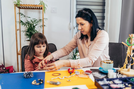 Mother and little preschooler daughters have fun making bracelets at home togetherの写真素材