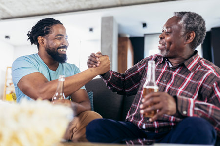 Excited old father and son watching tv,drink beer, having fun at homeの写真素材