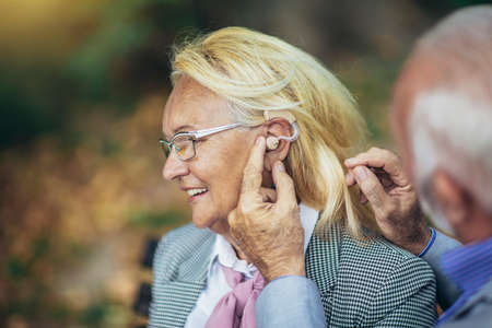 Senior couple with a hearing problem sitting on bench outdoorの写真素材