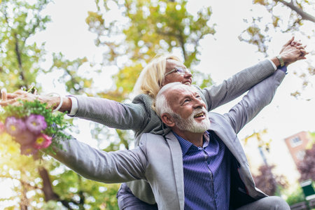 Senior man giving woman piggyback ride through parkの写真素材