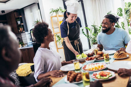 A multi-generational African-American family enjoying food at their dinner table. Caucasian woman...