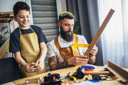 Father teaches young boy to plan wood in a carpentry workshop. Hobby and education concept