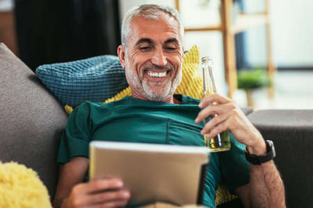 Mature man using tablet computer while relaxing on sofa at home