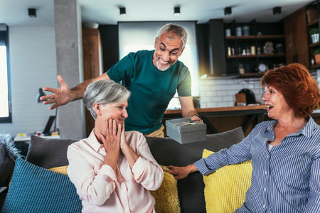 Group of middle age friends celebrate birthday giving gifts at homeの写真素材