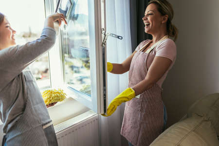 Mother and daughter child washing windows together. Girl helping woman do house cleaningの写真素材