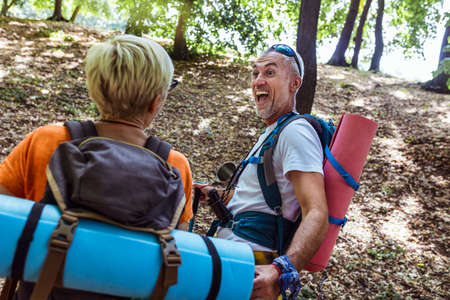 Senior couple hiking in forest wearing backpacks and hiking poles. Nordic walking, trekking. Healthy...