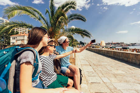 Happy mother, son and daughter together at seacoast with luggage backpack make selfie photo. Travel, tourism, family concept.の写真素材