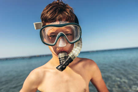 Portrait of a smiling little boy with scuba mask and snorkel by the seaの写真素材
