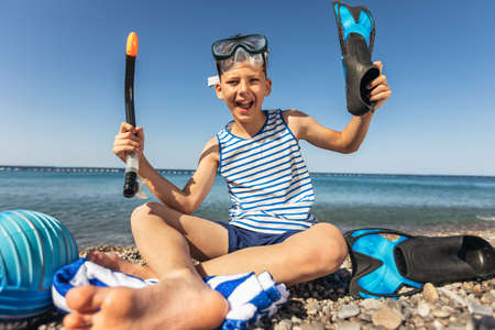 Happy boy has water polo ball and scuba gear on the beach. Looking at camera. Concept of travel, tourism, family.の写真素材