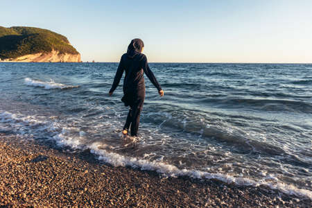 Woman in hijab standing on the beach looking at horizon