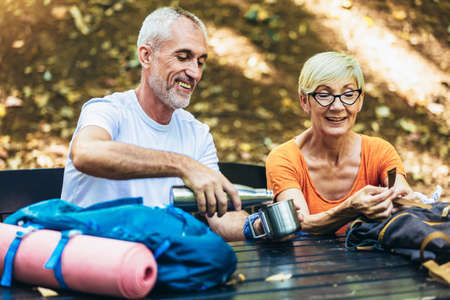 Mature couple sitting and drink coffee while resting in the forest after hiking.の写真素材
