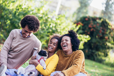 Beautiful young family lying on a picnic blanket with their dog, enjoying an autumn day in parkの写真素材