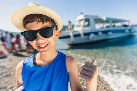 Portrait of a smiling boy on the beach with a tourist boat in the backgroundの写真素材
