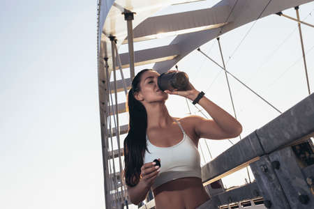 Fitness woman drinking water from bottle. Muscular young female taking a break from workout outside.の写真素材