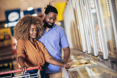 African American couple with trolley purchasing groceries at mallの写真素材