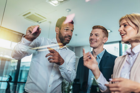 Young creative businessman standing with his colleagues writing new ideas on sticky notes over glass wallの写真素材