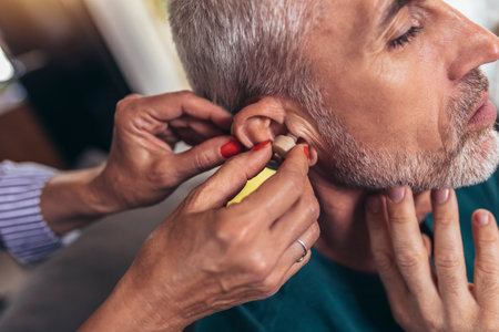 Woman helps mature male patient to use hearing aid.