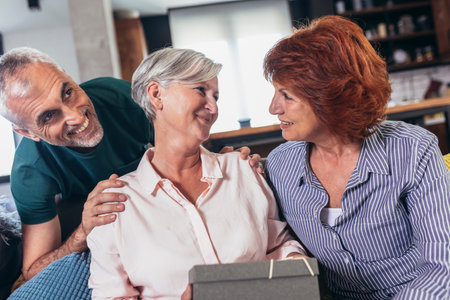 Group of middle age friends celebrate birthday giving gifts at home