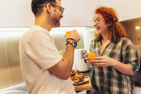Happy young couple enjoying fresh orange juice for a breakfast at homeの写真素材