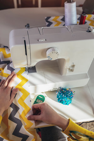 Woman sewing on a sewing machine at her home, close up.