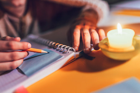 Little boy studying in low light with a burning candle. Close up.の写真素材