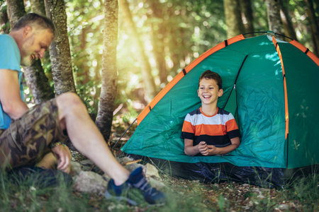 Father and son spending happy leisure time together outdoors in forest trees background. They are camping together and have funの写真素材