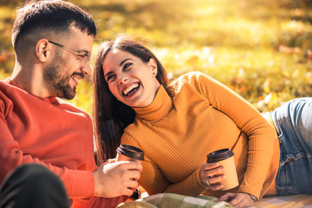 Young man and woman sit on a blanket in the park in autumn, drink coffee.の写真素材