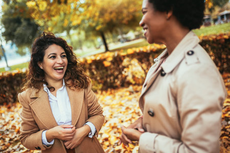 Happy woman friends walking in forest at autumn. They are chatting and having fun.の写真素材