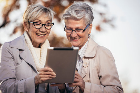 Two senior female friends using digital tablet in the parkの写真素材
