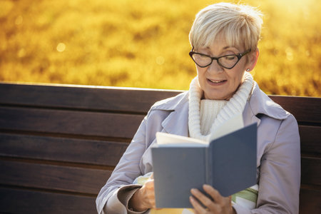 Senior woman relaxing in park with novelの写真素材