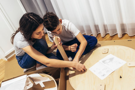 Brother and sister in casual clothing assembling furniture in apartmentの写真素材